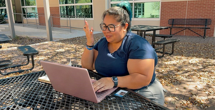 Person wearing glasses working outside on a laptop, seated in a group of picnic tables